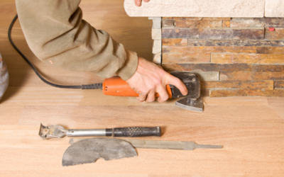 Technician carefully sanding hardwood floor near a fireplace.