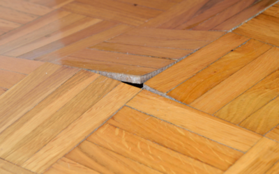 Wooden parquet floor with buckling, a sign of water damage, highlighting the need to repair or refinish hardwood floors.