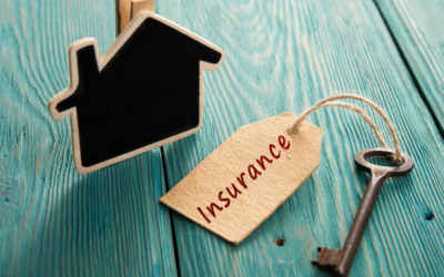 A house key sits atop a wood floor, with a tag about homeowner’s insurance attached to it.