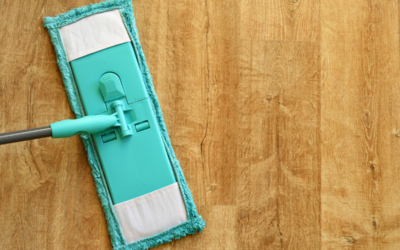 A blue-green mop with a reusable towel head being used to clean a hardwood floor.