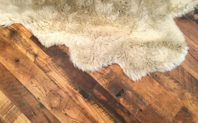 A sheepskin rug partially covering a section of hardwood floor with visible dark water stains and wear.